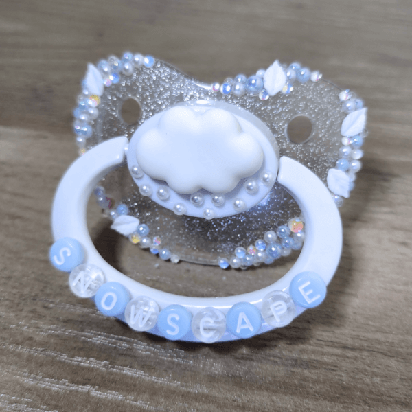 a silver and white snow themed paci with a cloud decoration
