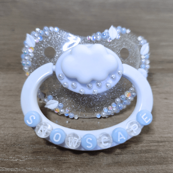 a silver and white snow themed paci with a cloud decoration