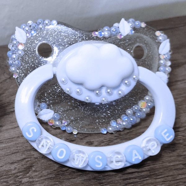 a silver and white snow themed paci with a cloud decoration