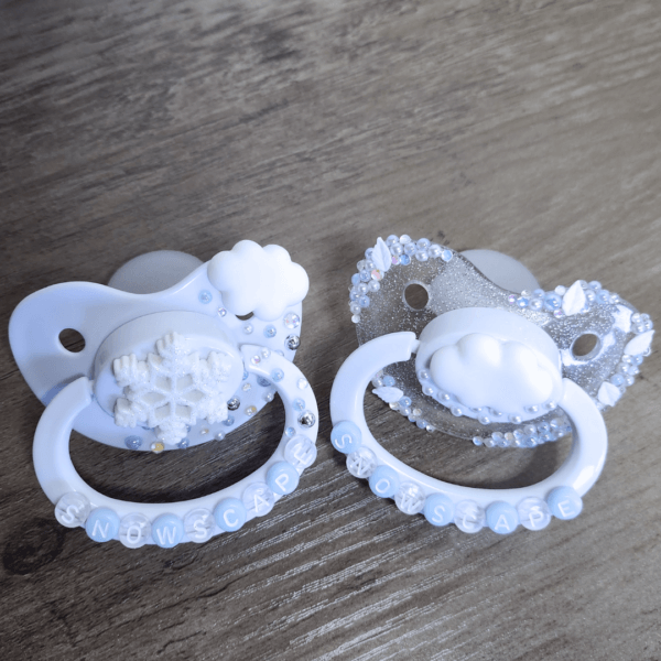 a silver and white snow themed paci and white paci with cloud and snowflake decorations