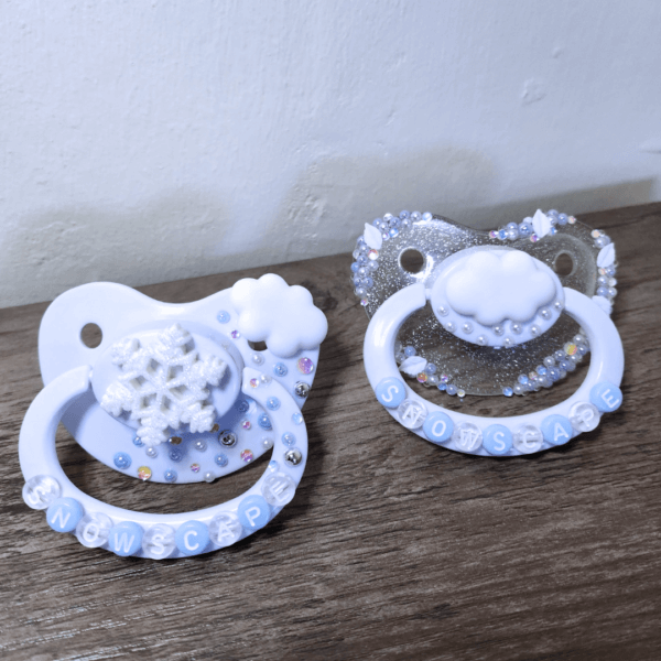 a silver and white snow themed paci and white paci with cloud and snowflake decorations